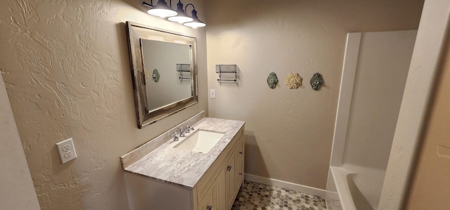 bathroom featuring baseboards, a bathtub, vanity, and a textured wall