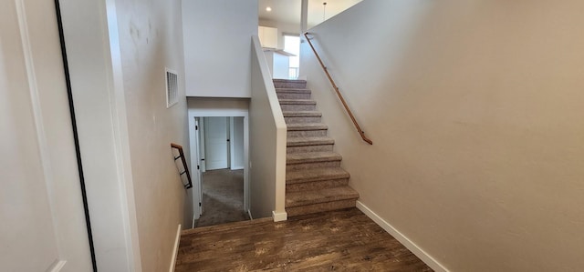 staircase featuring visible vents, baseboards, a high ceiling, and wood finished floors