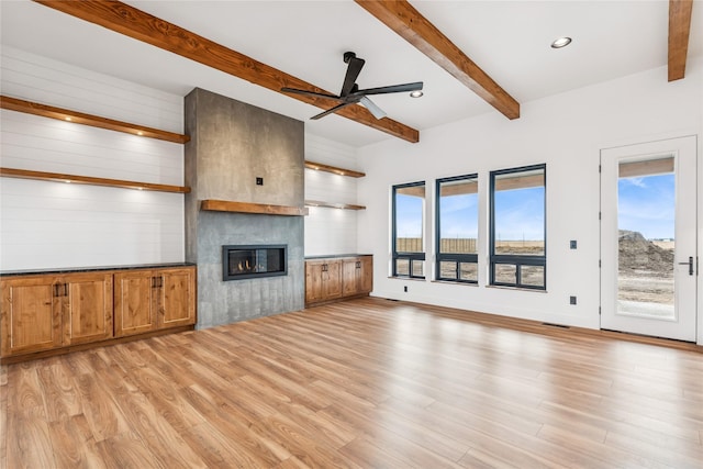 unfurnished living room featuring beam ceiling, light wood-style flooring, a wealth of natural light, and ceiling fan