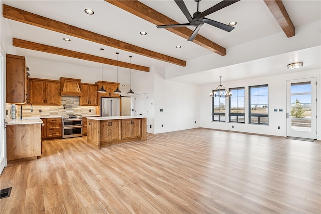 kitchen with custom exhaust hood, a sink, light countertops, appliances with stainless steel finishes, and ceiling fan with notable chandelier