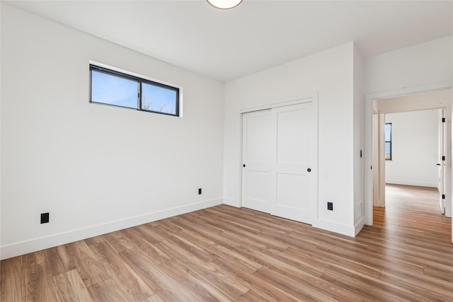 unfurnished bedroom featuring a closet, baseboards, and light wood-style flooring