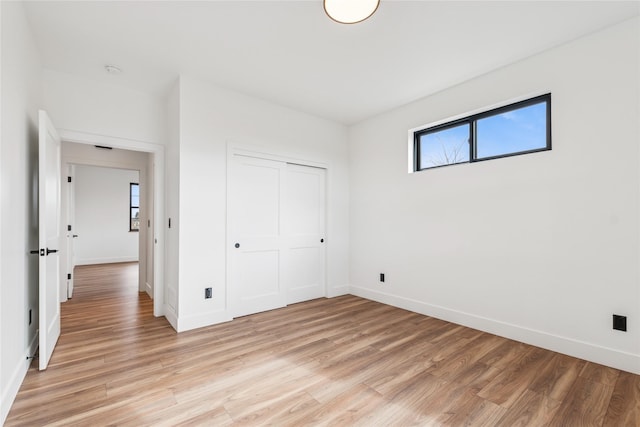 unfurnished bedroom with multiple windows, baseboards, and light wood-style floors