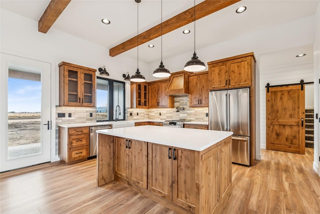 kitchen with a sink, custom range hood, appliances with stainless steel finishes, a barn door, and brown cabinets