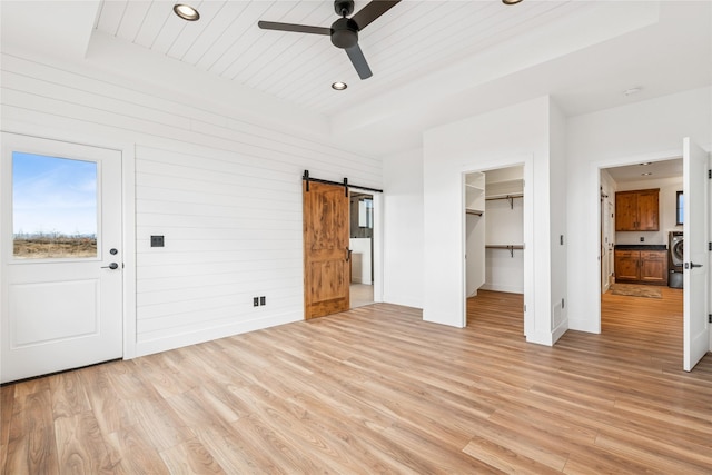 unfurnished bedroom featuring washer / dryer, light wood-style flooring, wood ceiling, and a barn door