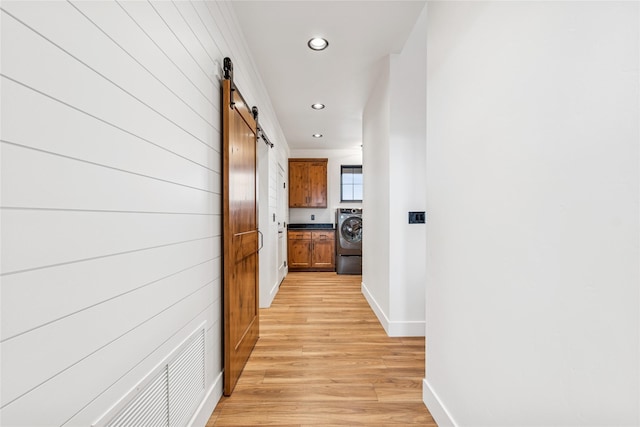 hallway with light wood-type flooring, washer / clothes dryer, recessed lighting, a barn door, and baseboards