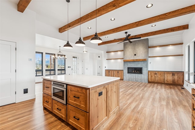 kitchen featuring pendant lighting, a center island, a large fireplace, light wood-style floors, and built in microwave