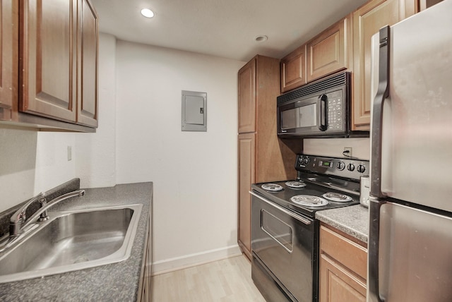 kitchen featuring black appliances, a sink, electric panel, light wood finished floors, and baseboards