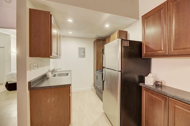 kitchen with a sink, electric panel, dark countertops, freestanding refrigerator, and light wood-style floors