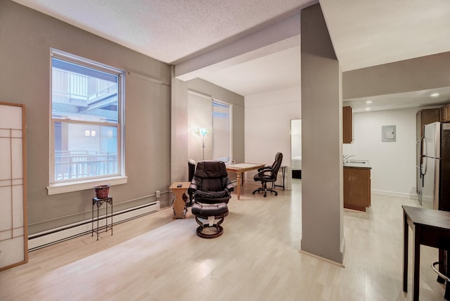 sitting room with a baseboard heating unit, light wood-style flooring, baseboards, and a textured ceiling