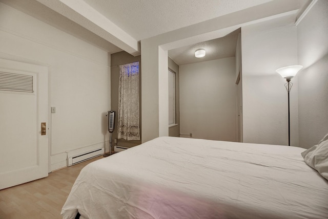 bedroom with baseboard heating, light wood-style flooring, and a textured ceiling