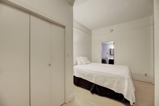 bedroom with baseboards, light wood finished floors, washer / dryer, a closet, and a textured ceiling