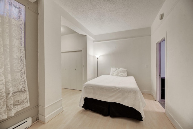 bedroom featuring a textured ceiling, light wood-type flooring, a baseboard heating unit, and baseboards