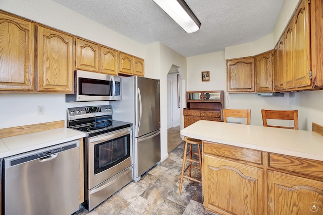 kitchen featuring brown cabinetry, a textured ceiling, stainless steel appliances, and light countertops