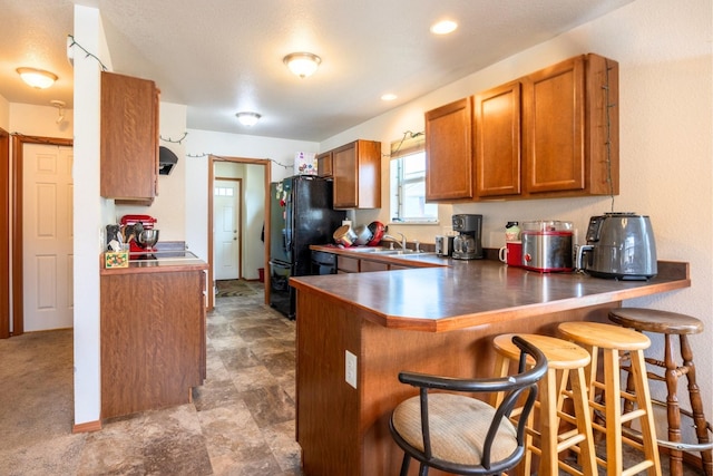 kitchen with a breakfast bar area, a peninsula, freestanding refrigerator, a sink, and brown cabinets