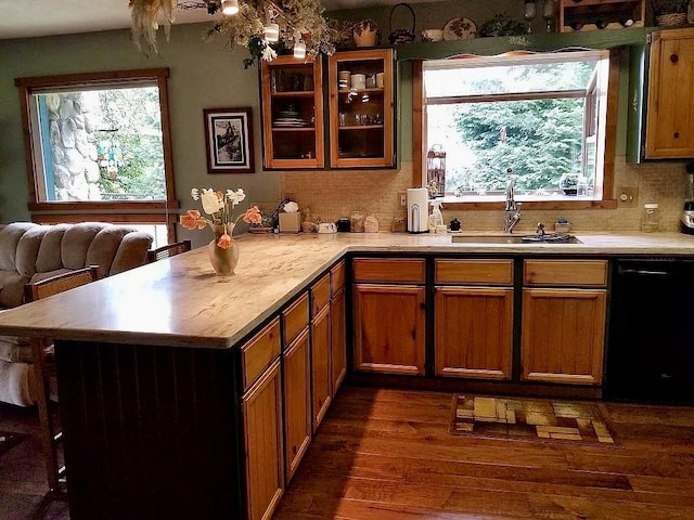 kitchen with dishwasher, light countertops, a peninsula, dark wood-style floors, and a sink