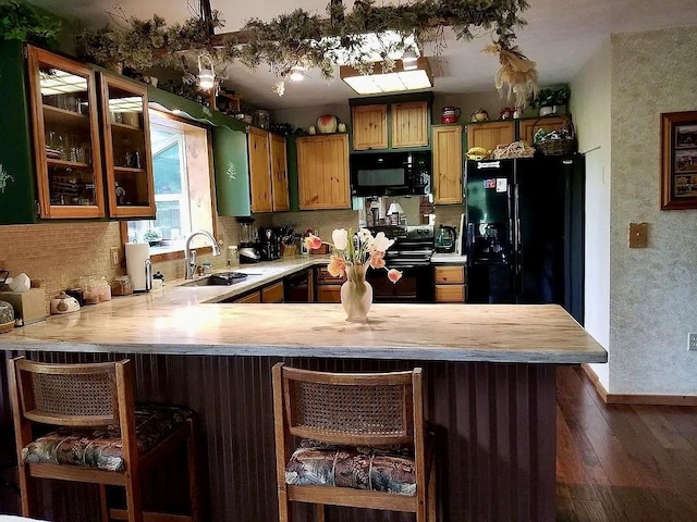 kitchen featuring dark wood finished floors, light countertops, a peninsula, black appliances, and a sink