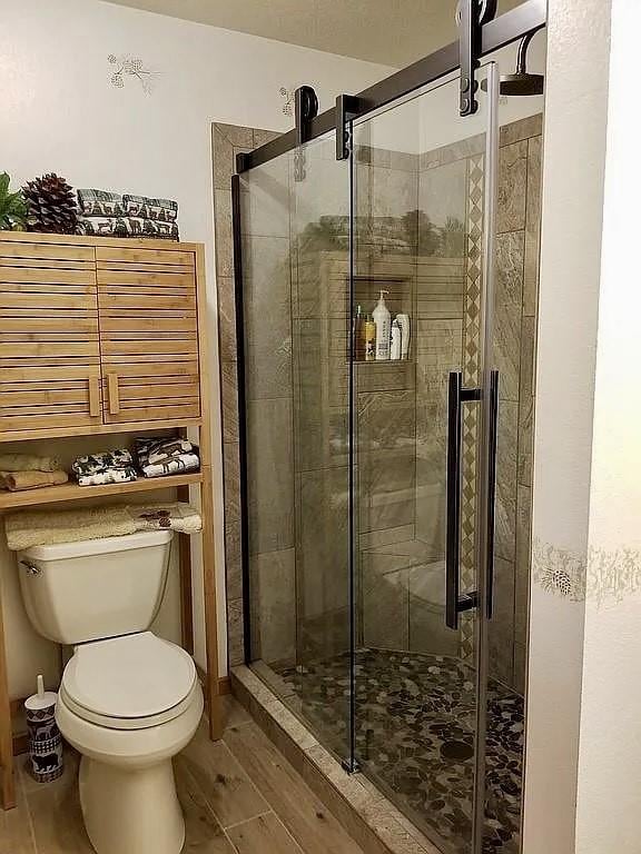 bathroom with toilet, wood finished floors, and a stall shower