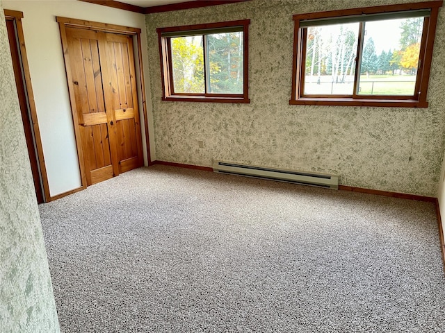 empty room featuring a baseboard heating unit, plenty of natural light, carpet, and baseboards