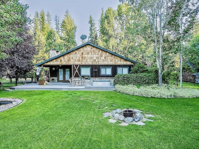 back of house with a chimney, french doors, a lawn, and a fire pit