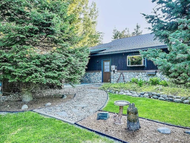 view of front of home featuring a front lawn, stone siding, roof with shingles, and a patio