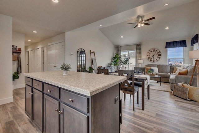 kitchen featuring light wood-style flooring, a ceiling fan, a center island, light countertops, and vaulted ceiling