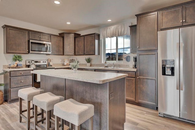 kitchen with light wood-style flooring, a center island, dark brown cabinetry, appliances with stainless steel finishes, and a breakfast bar area