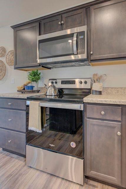 kitchen featuring light wood-type flooring, dark brown cabinetry, appliances with stainless steel finishes, and light countertops