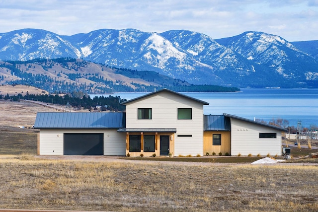 exterior space featuring a garage, driveway, a standing seam roof, metal roof, and a water and mountain view