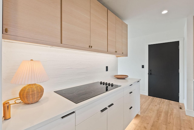 kitchen featuring light wood-style flooring, tasteful backsplash, recessed lighting, light countertops, and black electric stovetop