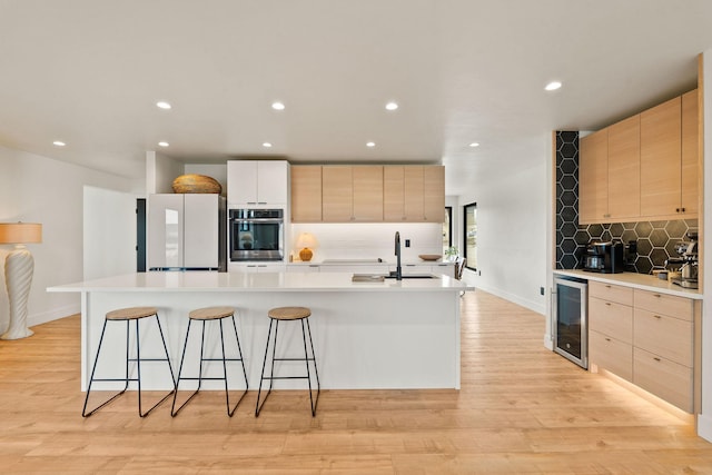 kitchen featuring beverage cooler, light brown cabinets, freestanding refrigerator, and a sink