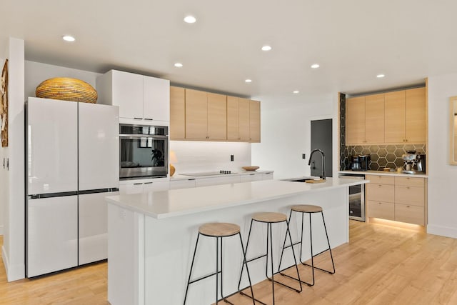 kitchen featuring stainless steel oven, light brown cabinetry, freestanding refrigerator, and a sink