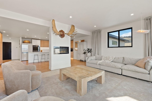 living area with recessed lighting, light wood-style flooring, and a glass covered fireplace