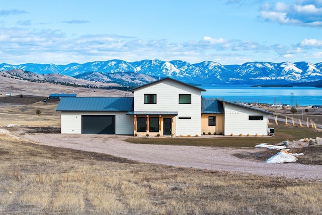 view of front of house with a standing seam roof, dirt driveway, an attached garage, metal roof, and a water and mountain view