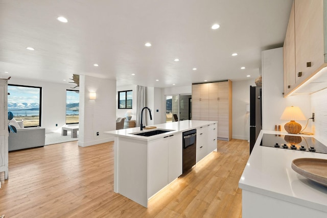 kitchen with light wood-type flooring, modern cabinets, black appliances, a center island with sink, and a sink