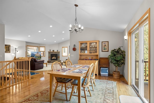 dining area featuring light wood-style flooring, a chandelier, a glass covered fireplace, and vaulted ceiling