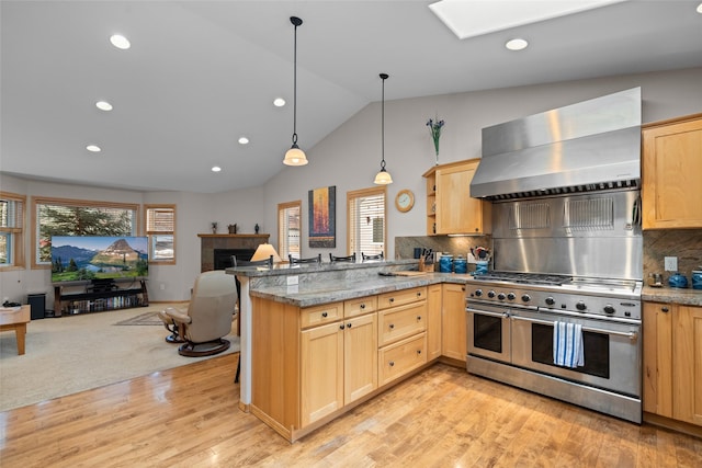 kitchen featuring range with two ovens, wall chimney exhaust hood, light brown cabinets, and open floor plan