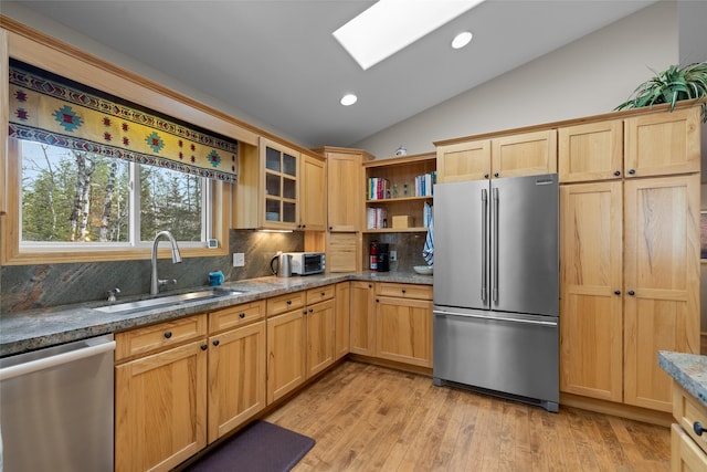 kitchen with light wood finished floors, a sink, appliances with stainless steel finishes, lofted ceiling with skylight, and backsplash