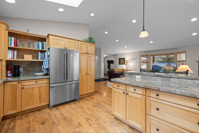 kitchen with light wood-type flooring, light brown cabinetry, light stone counters, vaulted ceiling with skylight, and high end refrigerator