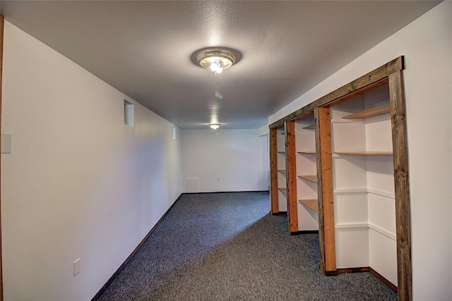 finished below grade area with dark carpet, a textured ceiling, and baseboards