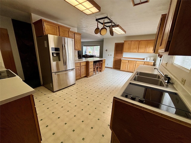 kitchen with brown cabinets, stainless steel refrigerator with ice dispenser, a sink, light countertops, and light floors