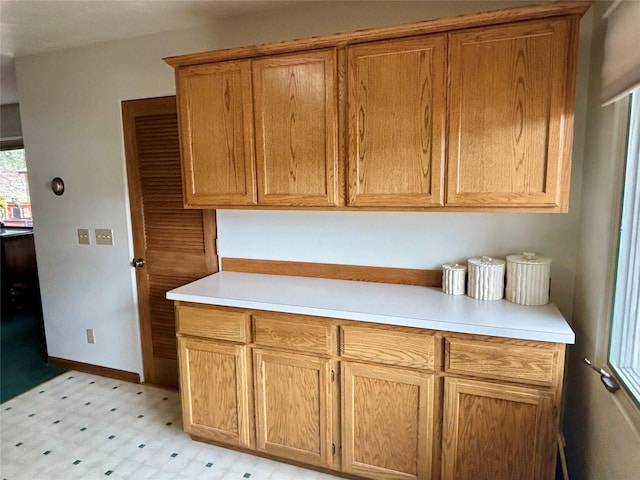 kitchen featuring brown cabinetry, light floors, light countertops, and baseboards