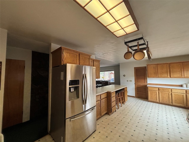 kitchen with light floors, light countertops, brown cabinets, a peninsula, and stainless steel fridge