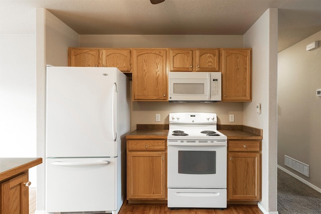 kitchen featuring visible vents, dark countertops, a textured ceiling, white appliances, and baseboards