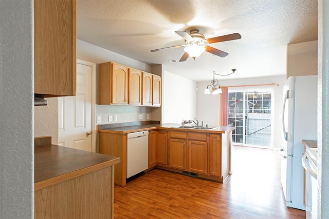 kitchen with white appliances, wood finished floors, a peninsula, a sink, and ceiling fan with notable chandelier