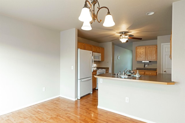 kitchen with ceiling fan with notable chandelier, light wood-style flooring, a peninsula, white appliances, and a sink