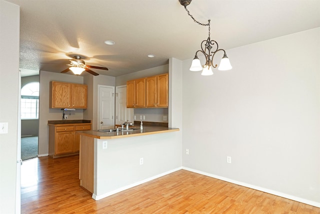 kitchen featuring a peninsula, baseboards, light wood finished floors, and a sink