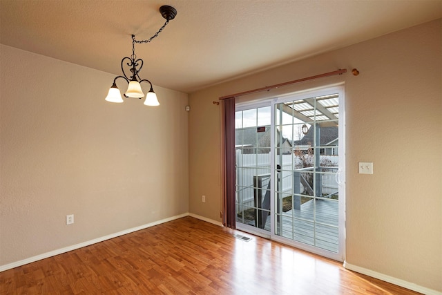 unfurnished dining area with visible vents, baseboards, an inviting chandelier, and wood finished floors