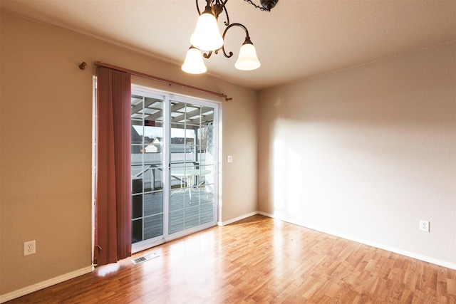 empty room featuring visible vents, light wood-style flooring, baseboards, and an inviting chandelier