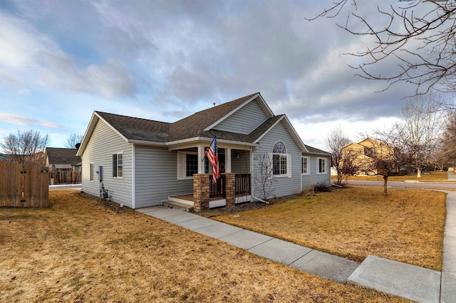 view of front of home featuring roof with shingles, a porch, a front lawn, and fence