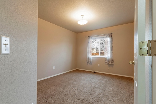 carpeted spare room with a textured ceiling and baseboards